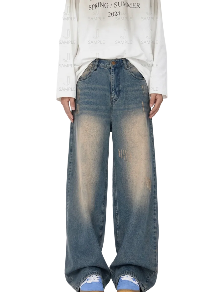 A person wearing wide-leg faded blue denim jeans with a white long-sleeve shirt and blue sneakers, standing against a white background with a repeating watermark pattern.